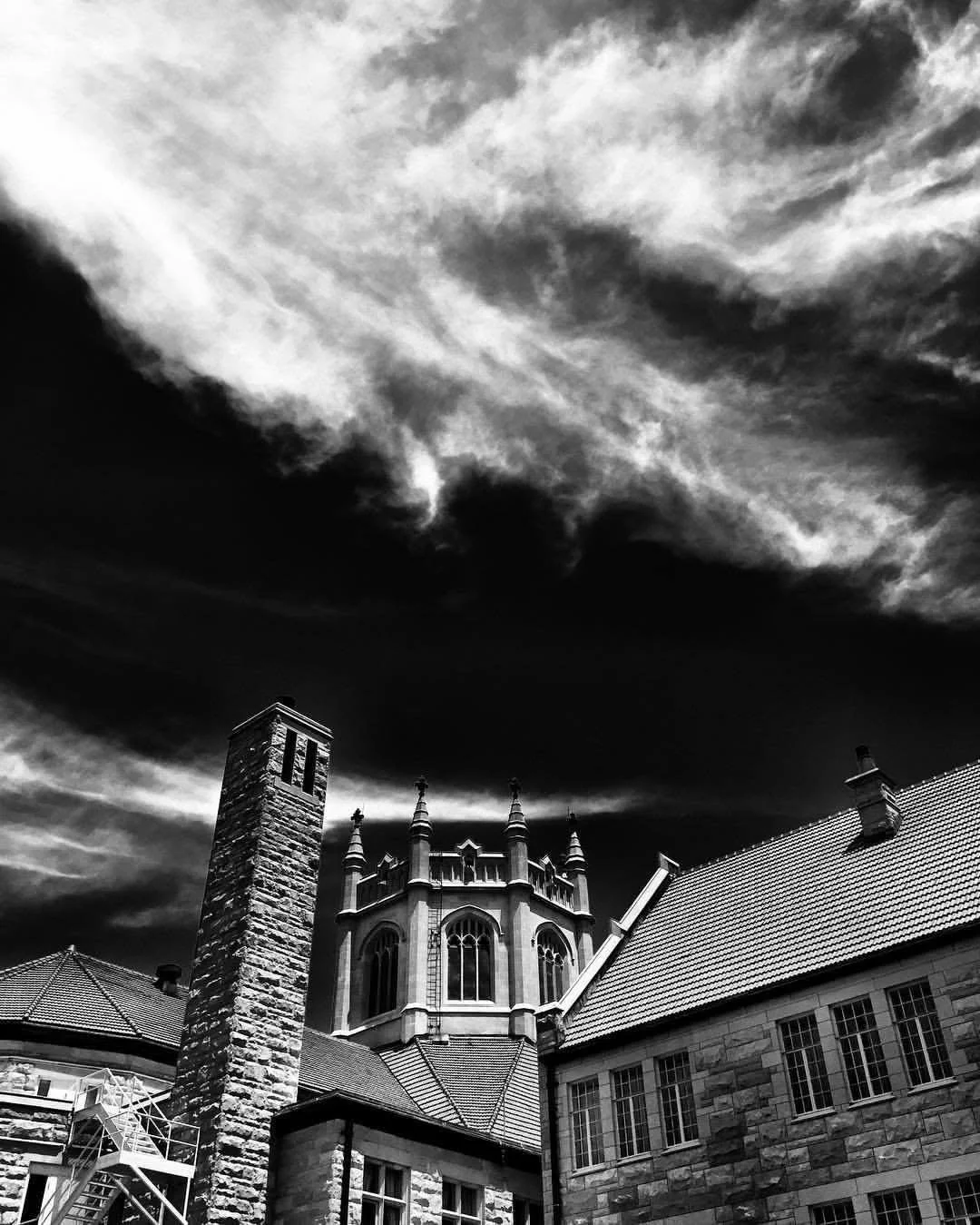 Black and white photo of a historic building with a spire and chimney against a cloudy sky.