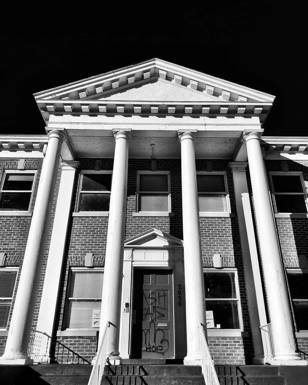 Front view of a large brick house with brick columns, a portico, and a triangular pediment, black-and-white photograph.