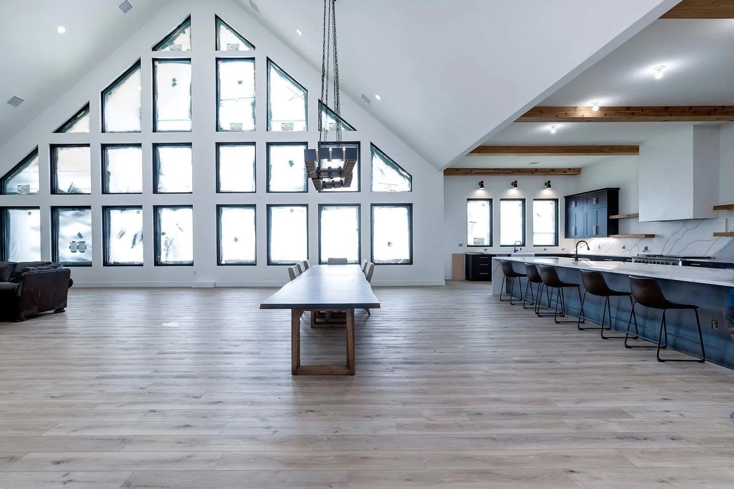 Modern, spacious open-concept living room and kitchen with high ceiling, large triangular windows, and wooden accents.