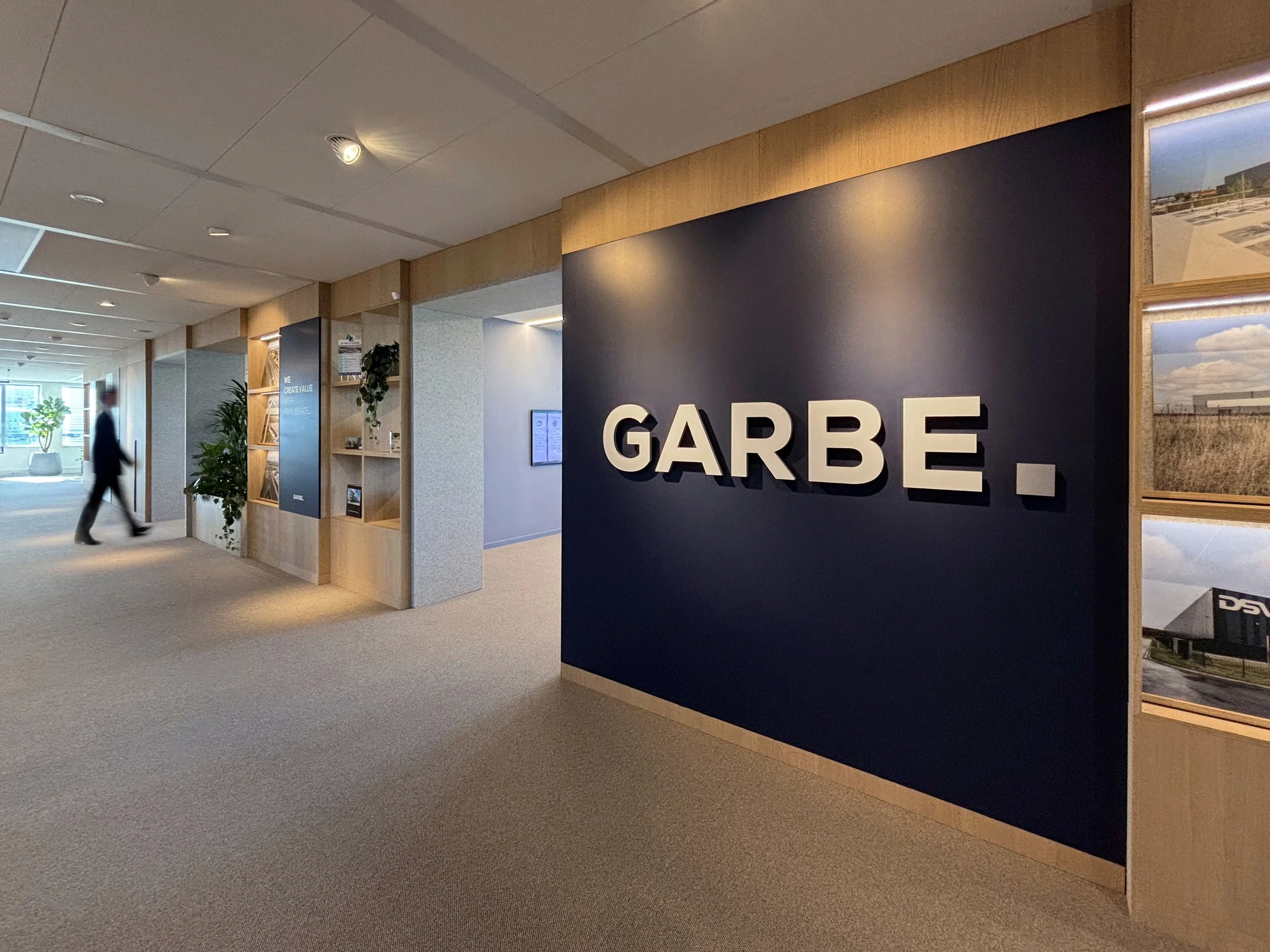 Office hall with Garbe logo wall and person walking at Garbe Institutional, Zuidas Amsterdam, designed by Meeder Ontwerpers.