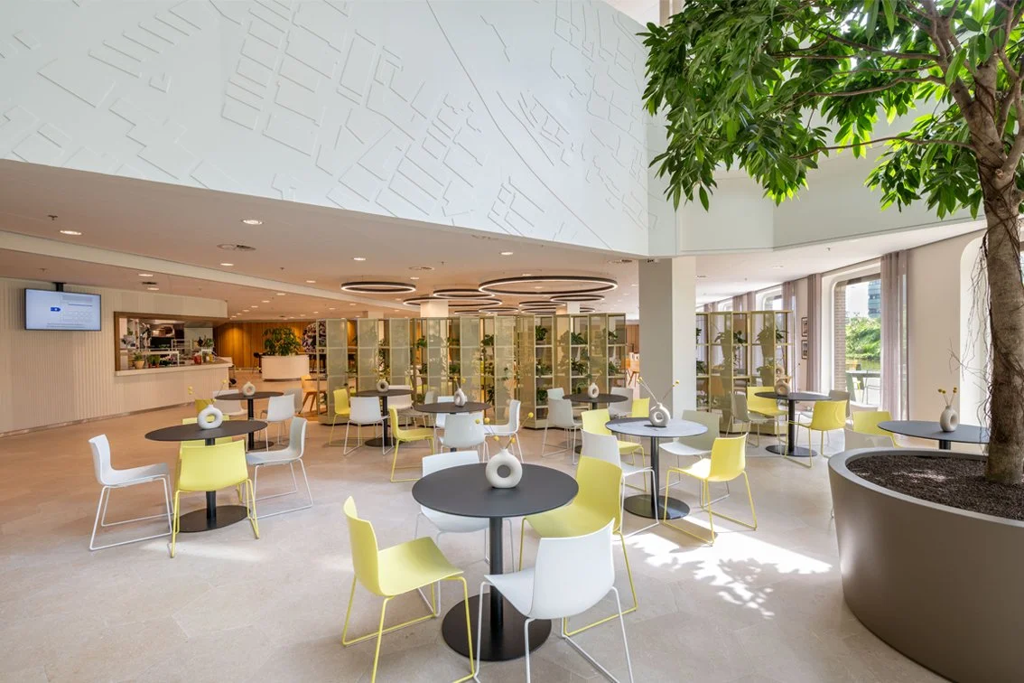 Atrium with indoor terrace, tree and yellow chairs in The Tasting Room at Rabobank Headquarters Utrecht, designed by Meeder Ontwerpers X OIII Architecten.