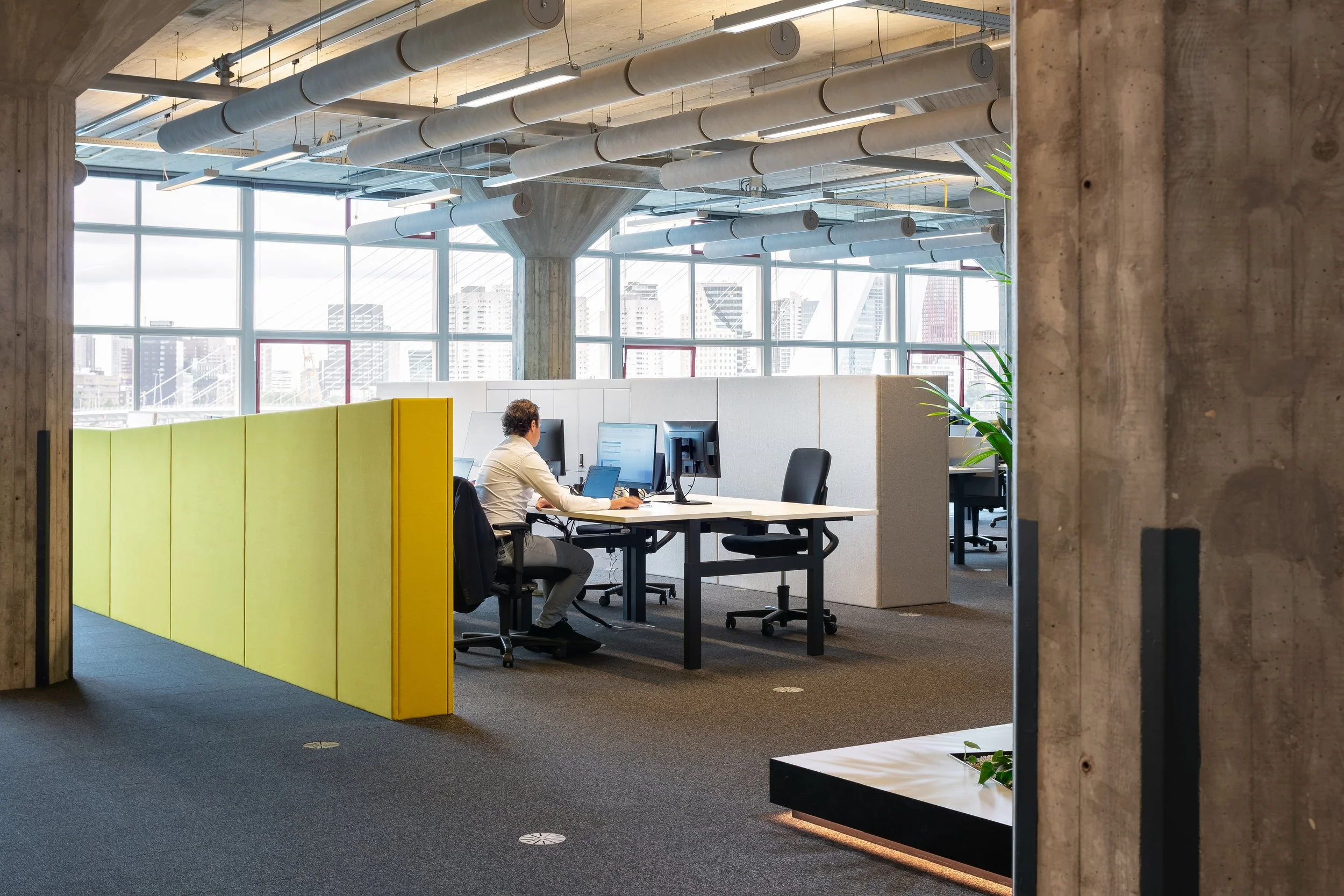Yellow workspace with textured wall and Erasmus Bridge view at Yuki HQ, Rotterdam, designed by Meeder Ontwerpers.