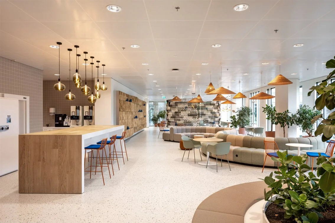 Bar table with round benches, woven pendant lamps and plants in The Garden Room at Rabobank Headquarters, Utrecht, designed by Meeder Ontwerpers.