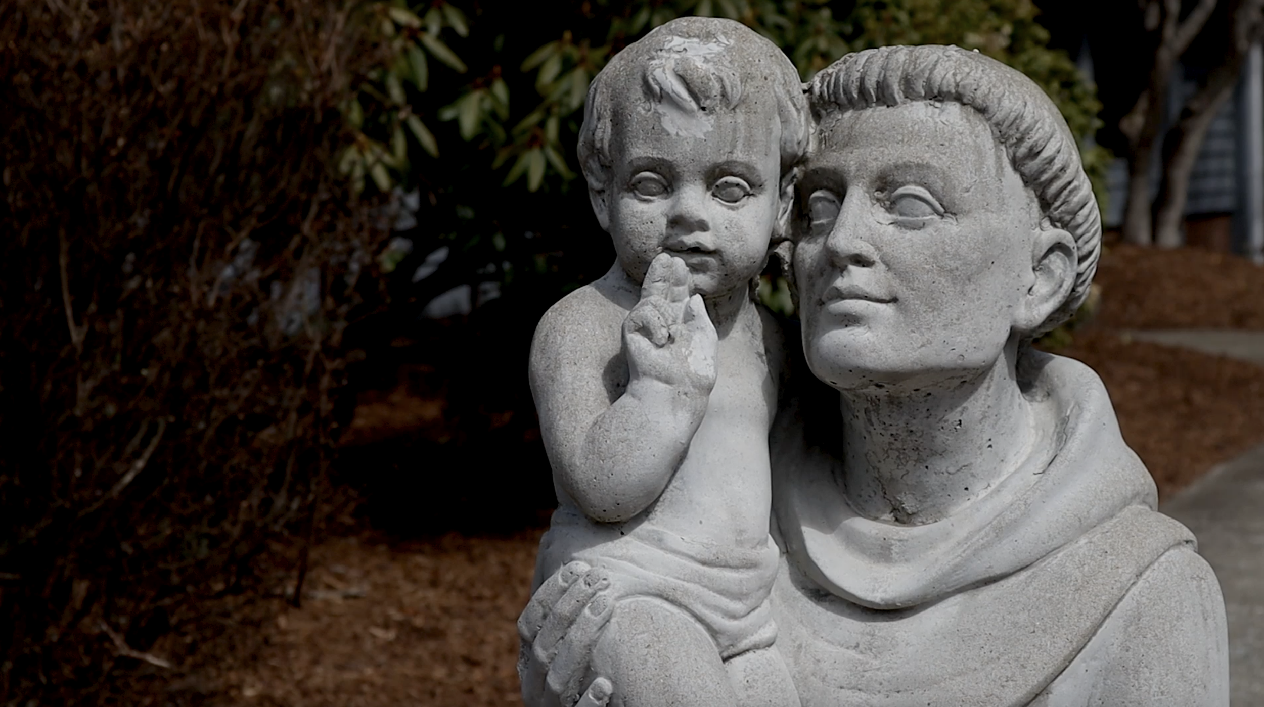 A stone sculpture set outdoors near bushes and trees.