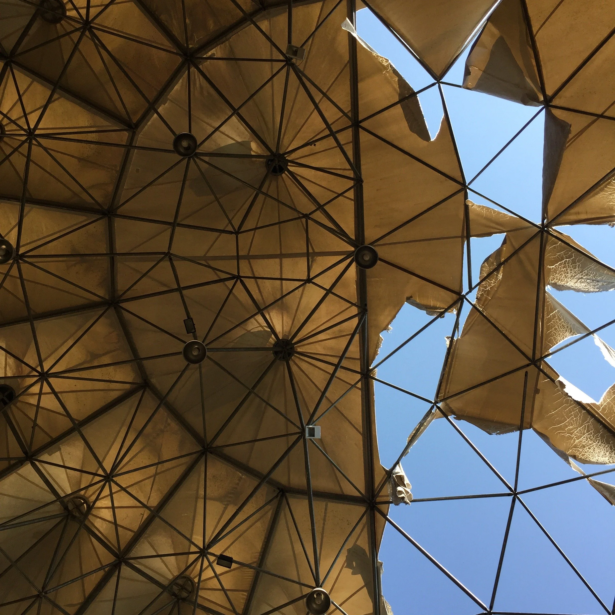Geometric fabric ceiling with damaged sections and sky visible through gaps