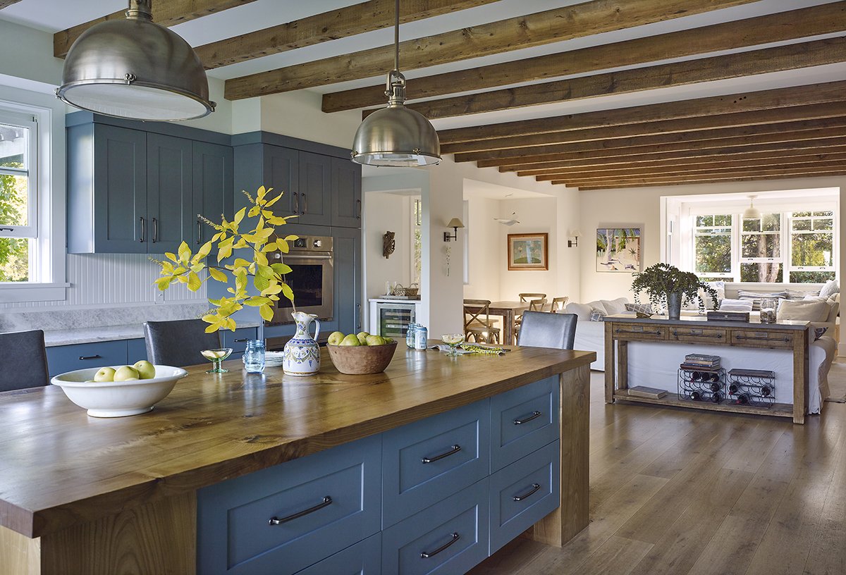 Modern kitchen with blue cabinets and wooden island, pendant lights, open to living area with light-filled windows.