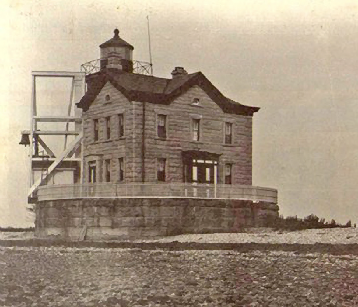 Historic lighthouse building with stone facade and small tower on a rocky shore