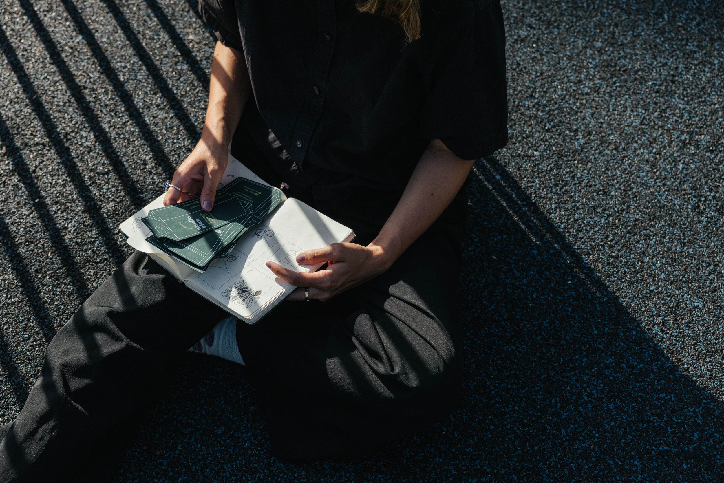 Skizzenbuch und Flyer von studioelan die von weiblichen Händen im Sonnenlicht gezeigt werden