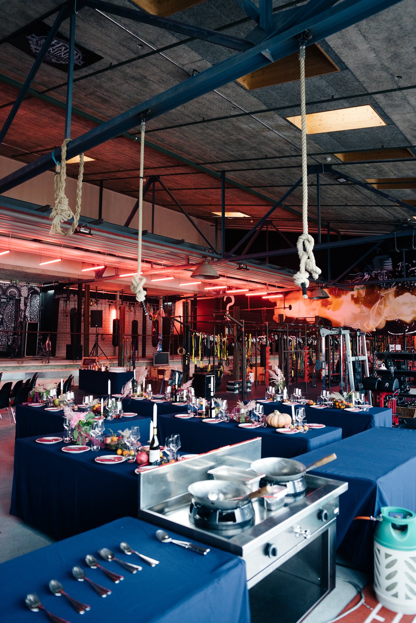 Festtafel mit bunten Früchten und frischen Blumen auf dunkelblauem Tischtusch und mit roten Neonleuchten im Hintergrund, Raumübersicht mit Seilen