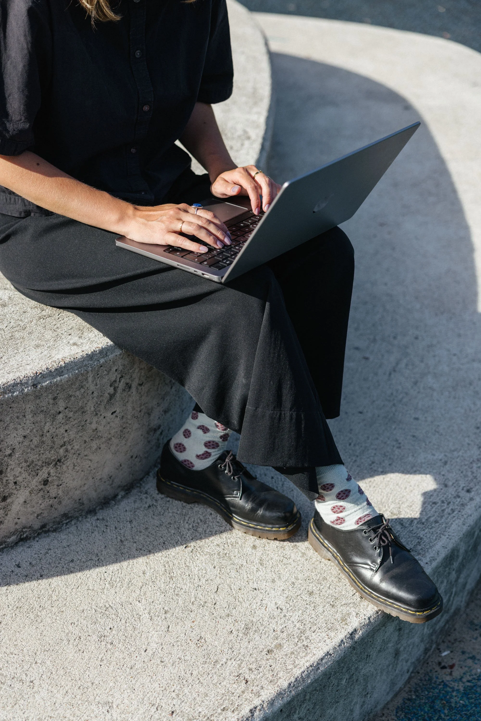 Laptop von Frau in dunkler Kleidung gehalten, Person sitzend auf Betontreppe in Sonnenlicht