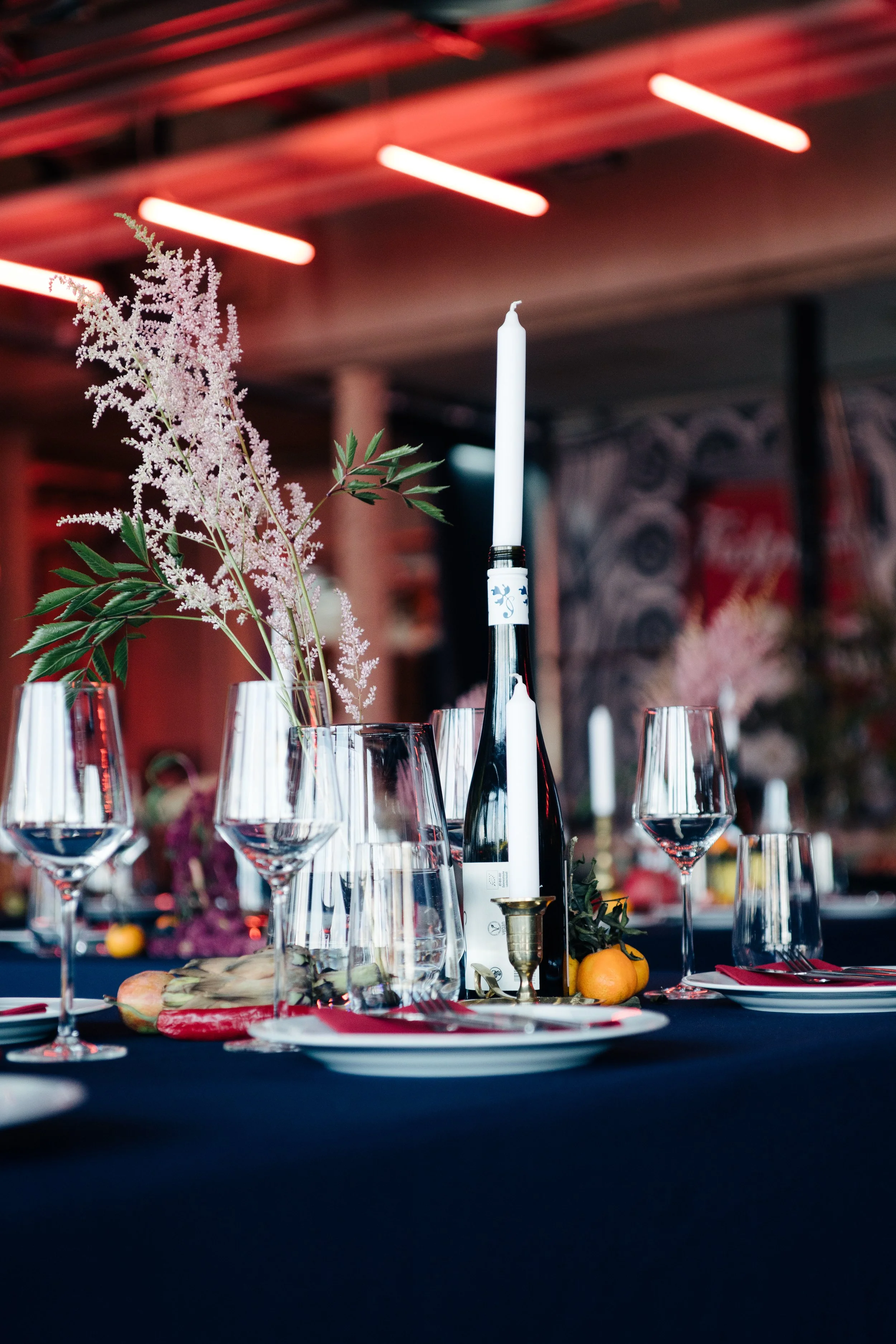 Festtafel mit bunten Früchten und frischen Blumen auf dunkelblauem Tischtusch und mit roten Neonleuchten im Hintergrund
