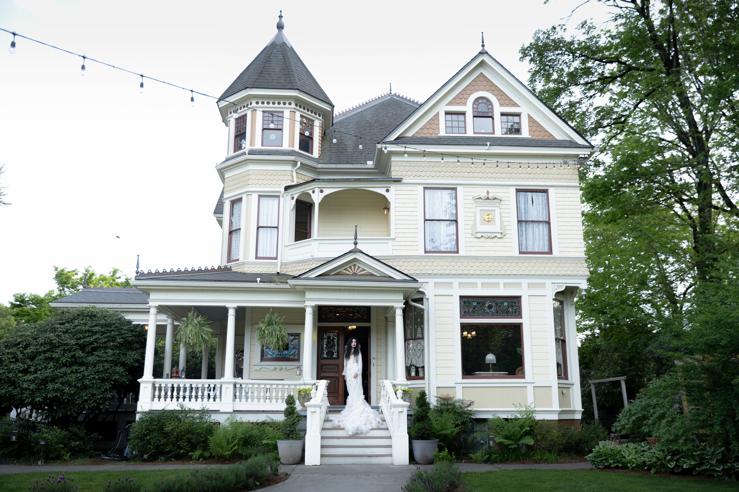 Victorian-style house with a tower, decorated for a wedding with a woman in a wedding dress on the front steps. Luxury Oregon Wedding Photographer. Wedding Inspo. Elevated Moody Editorial