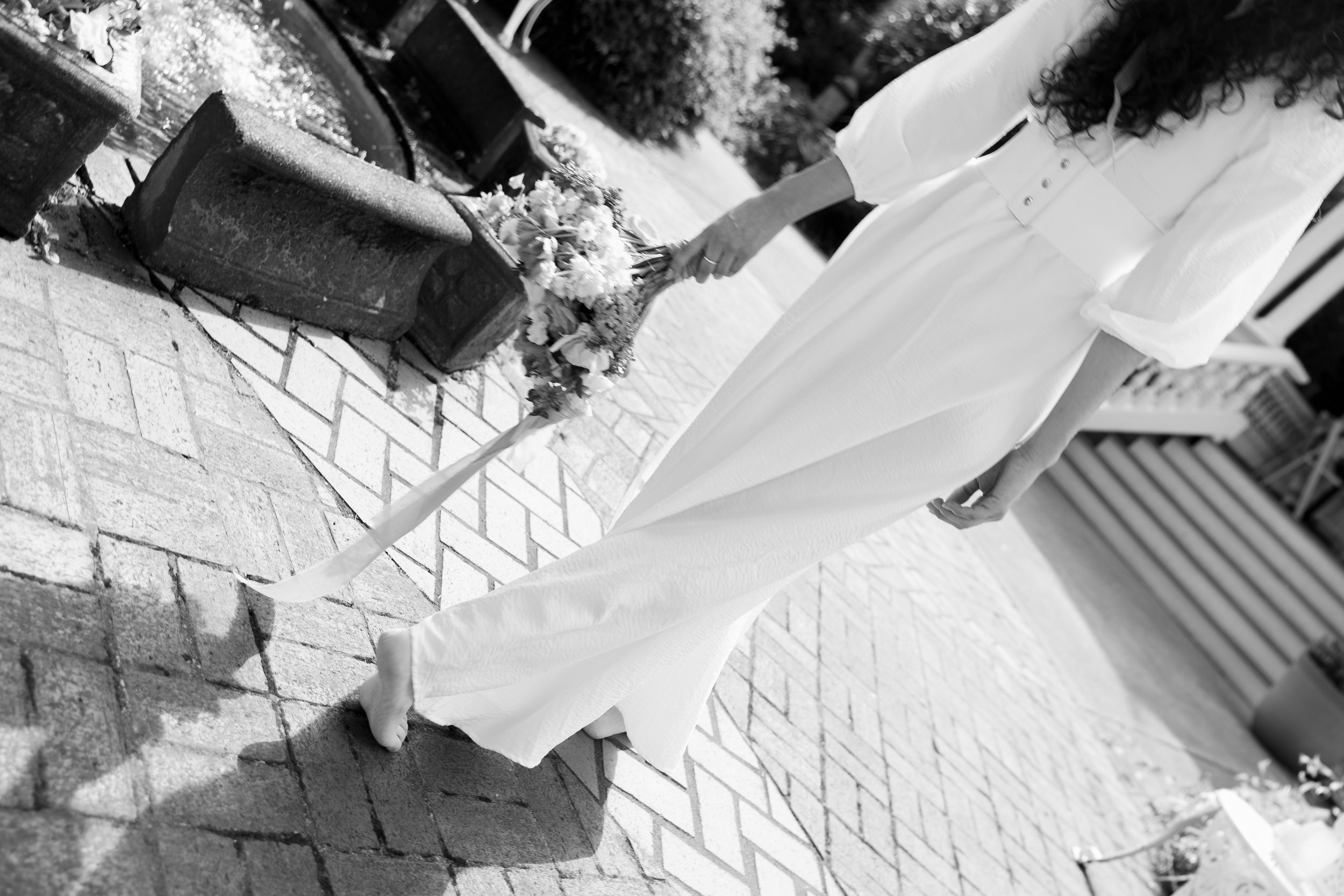 Person in white dress laying a white cloth over a brick sidewalk near a flower-covered grave site with a cross and flowers. Luxury Oregon Wedding Photographer. Wedding Inspo. Elevated Moody Editorial
