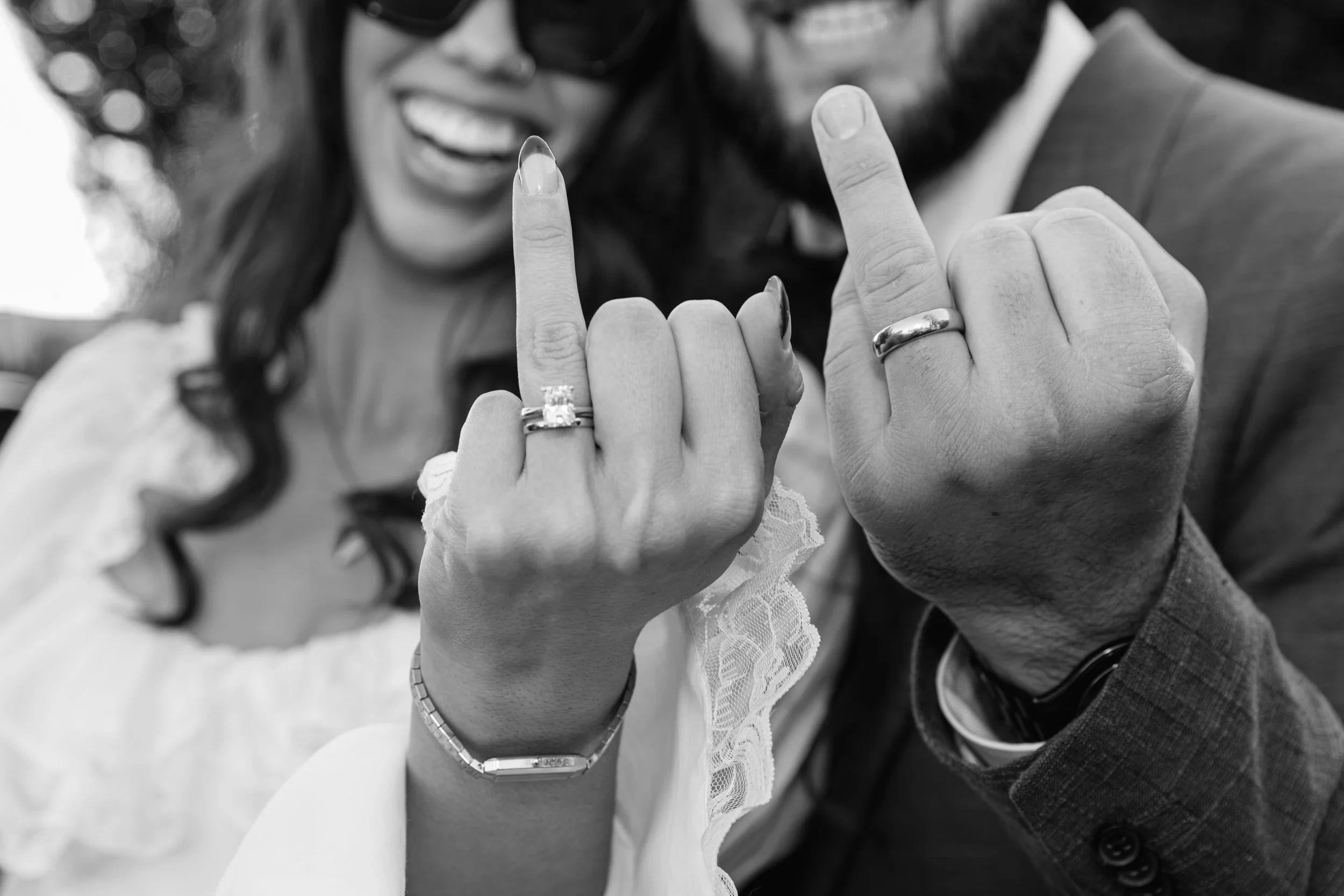 Close-up of two people showing a matching hand gesture with their pinky fingers, smiling, wearing rings and jewelry, in black and white.