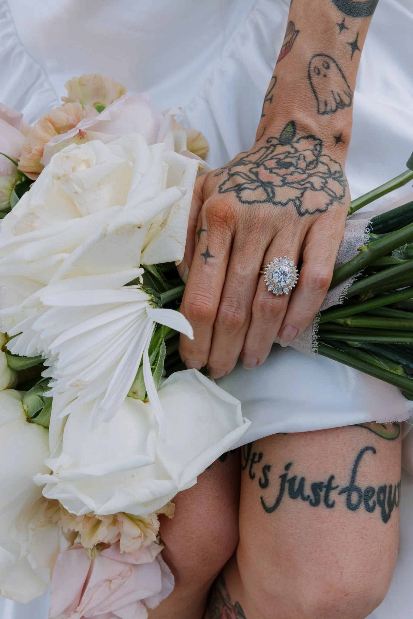 Close-up of two tattooed hands holding a bouquet of white and light pink flowers, with a wedding ring on the ring finger of one hand. Luxury wedding, Best Wedding Photographer, Oregon Wedding Photographer, Bay Area Wedding Photographer, California