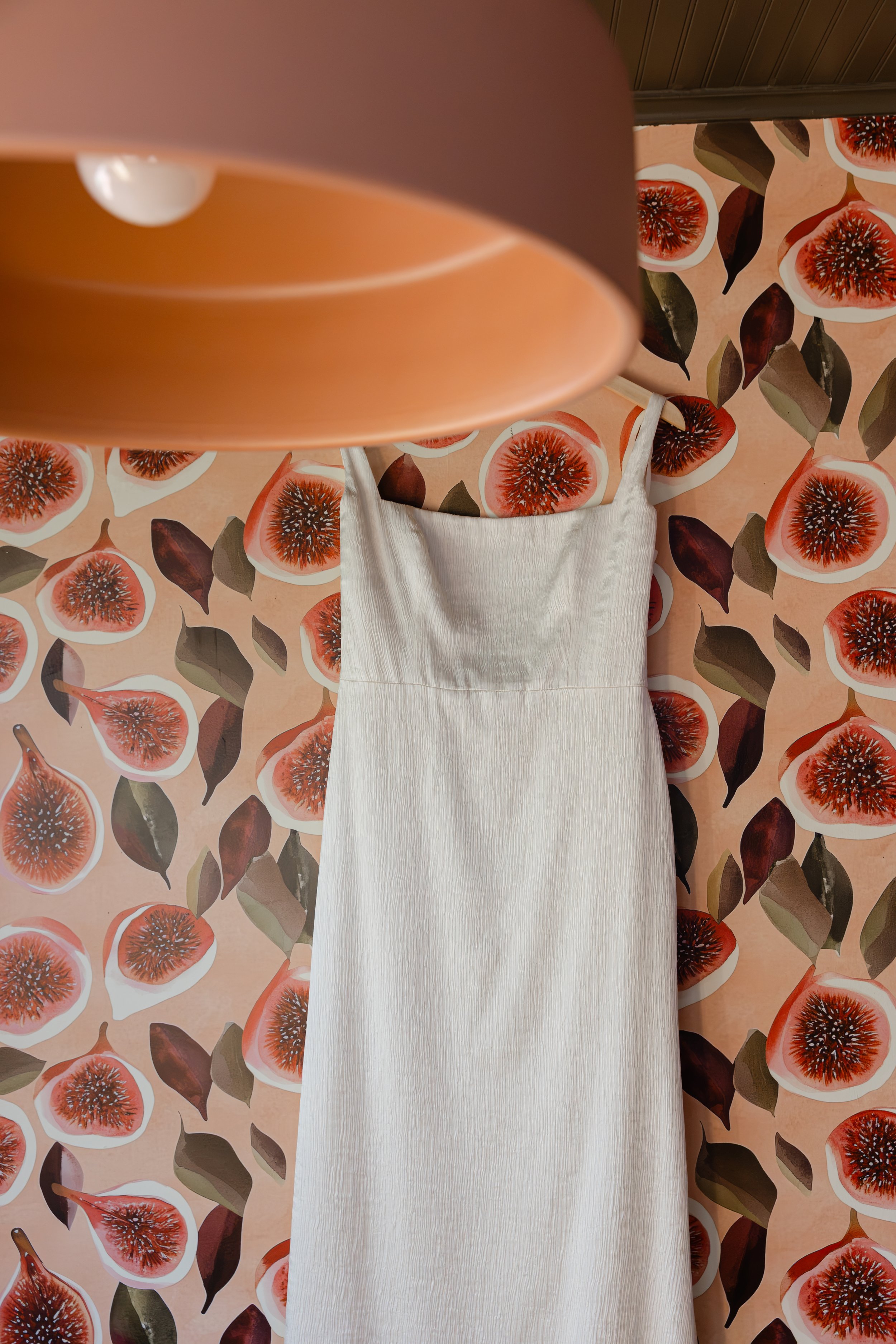 A white dress hanging against a background with a repeating pattern of sliced figs and leaves. Wedding Details Photography, Wedding Dress, Luxury Wedding Photography, Bay Area Wedding Photographer,Oregon wedding photographer, best wedding photography