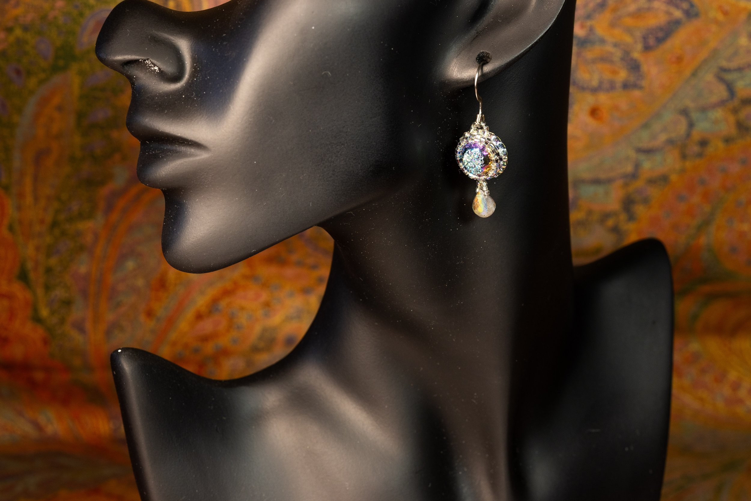 A black mannequin head wearing a sparkling, multicolored dangle earring.