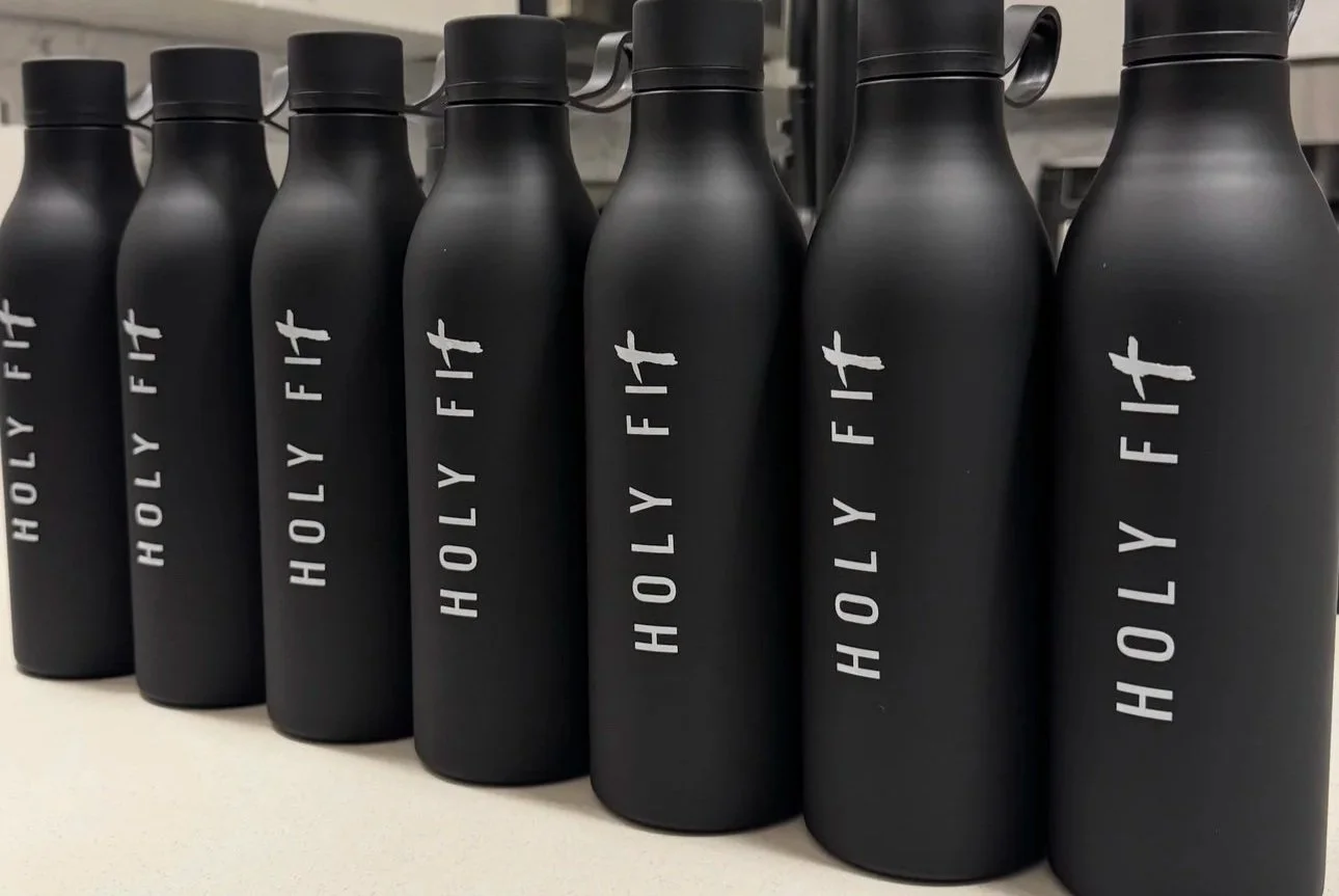 Black water bottles with white text reading 'Holy Fit' on a white surface.