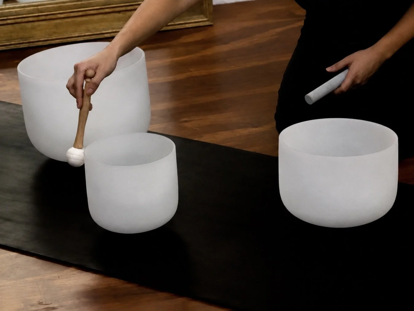 Dos personas tocando campanas de cristal o koshi de cristal en una mesa negra. Una persona sostiene un mazo con una cabeza blanca y la otra persona sostiene un mazo con mango gris.