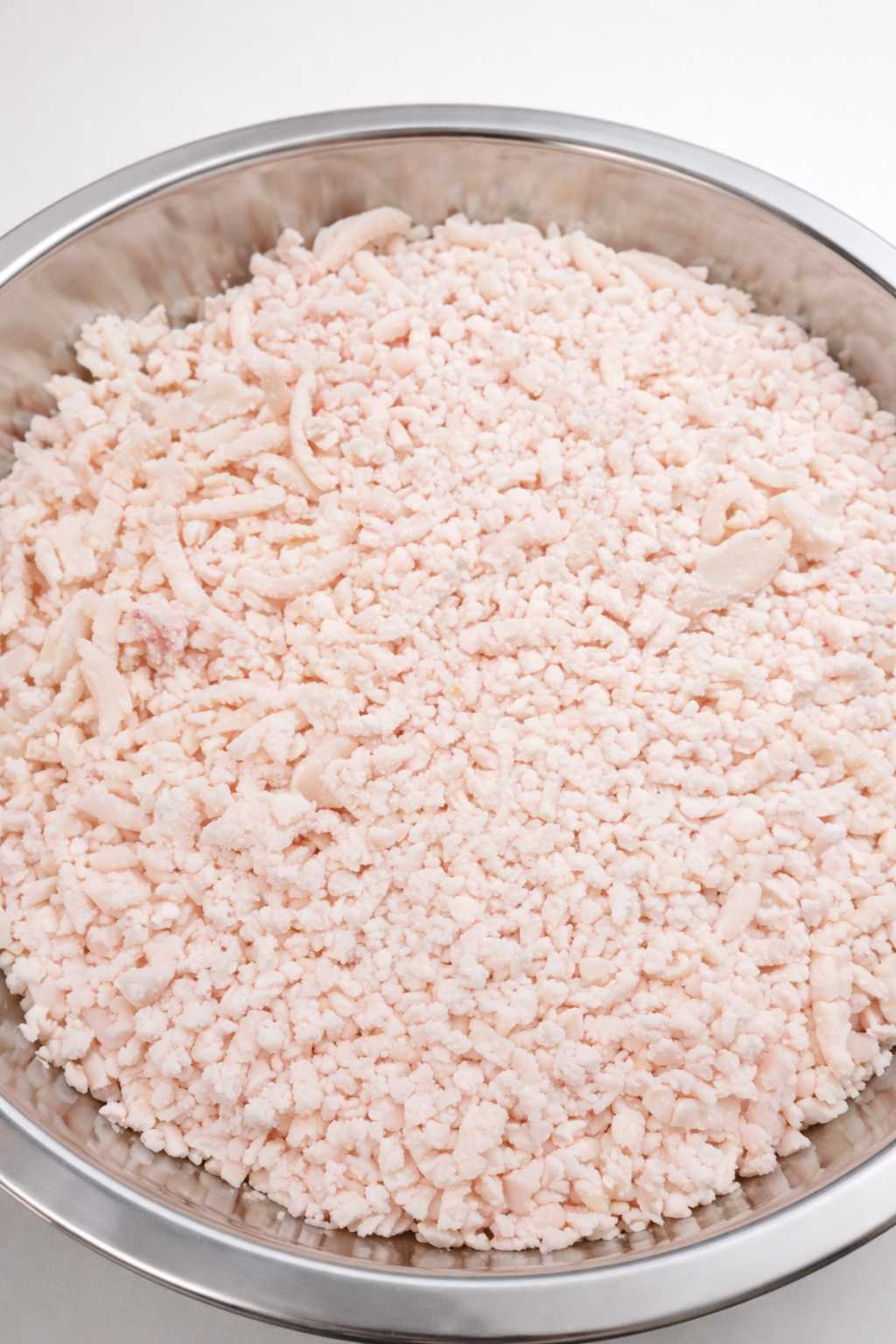 Close-up of a large metal bowl filled with shredded and crumbled cooked chicken.