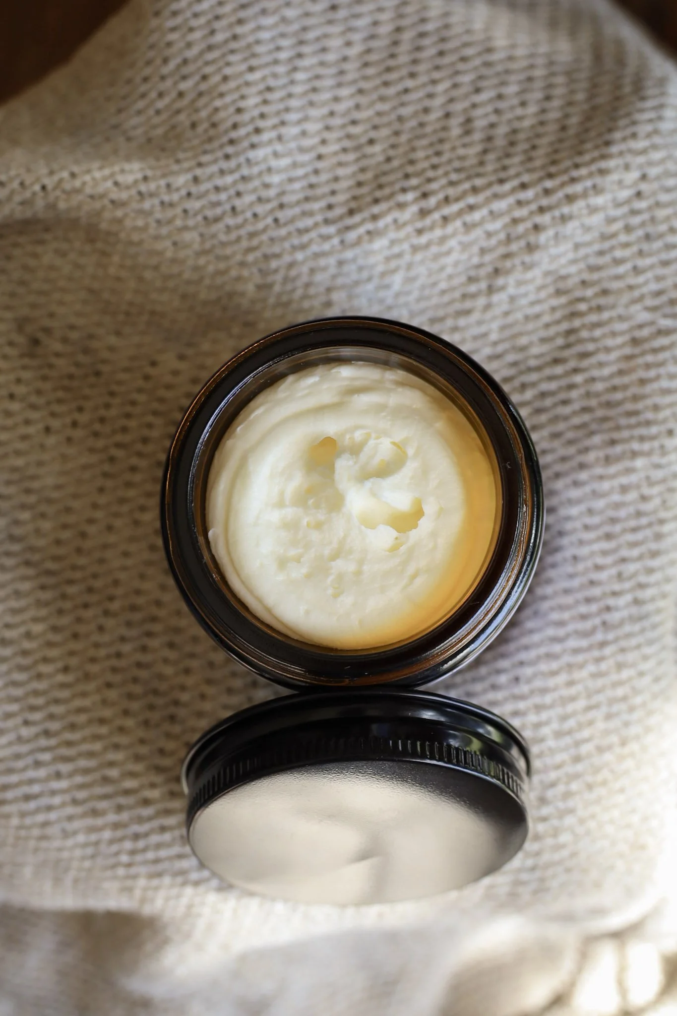 Open jar of creamy white substance on beige fabric background.