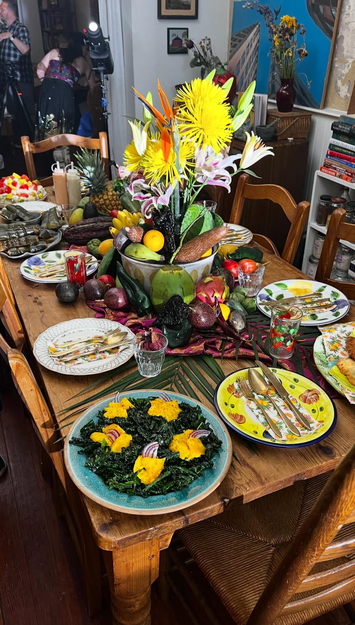 A dinner table decorated with a large floral centerpiece and a variety of colorful dishes, including a kale salad with yellow and purple toppings, set in a cozy, well-decorated dining room.