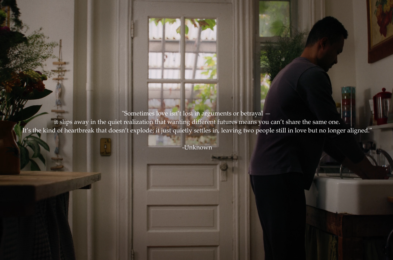 A man washing dishes at a kitchen sink with a door and window behind him, surrounded by houseplants and kitchen decor.