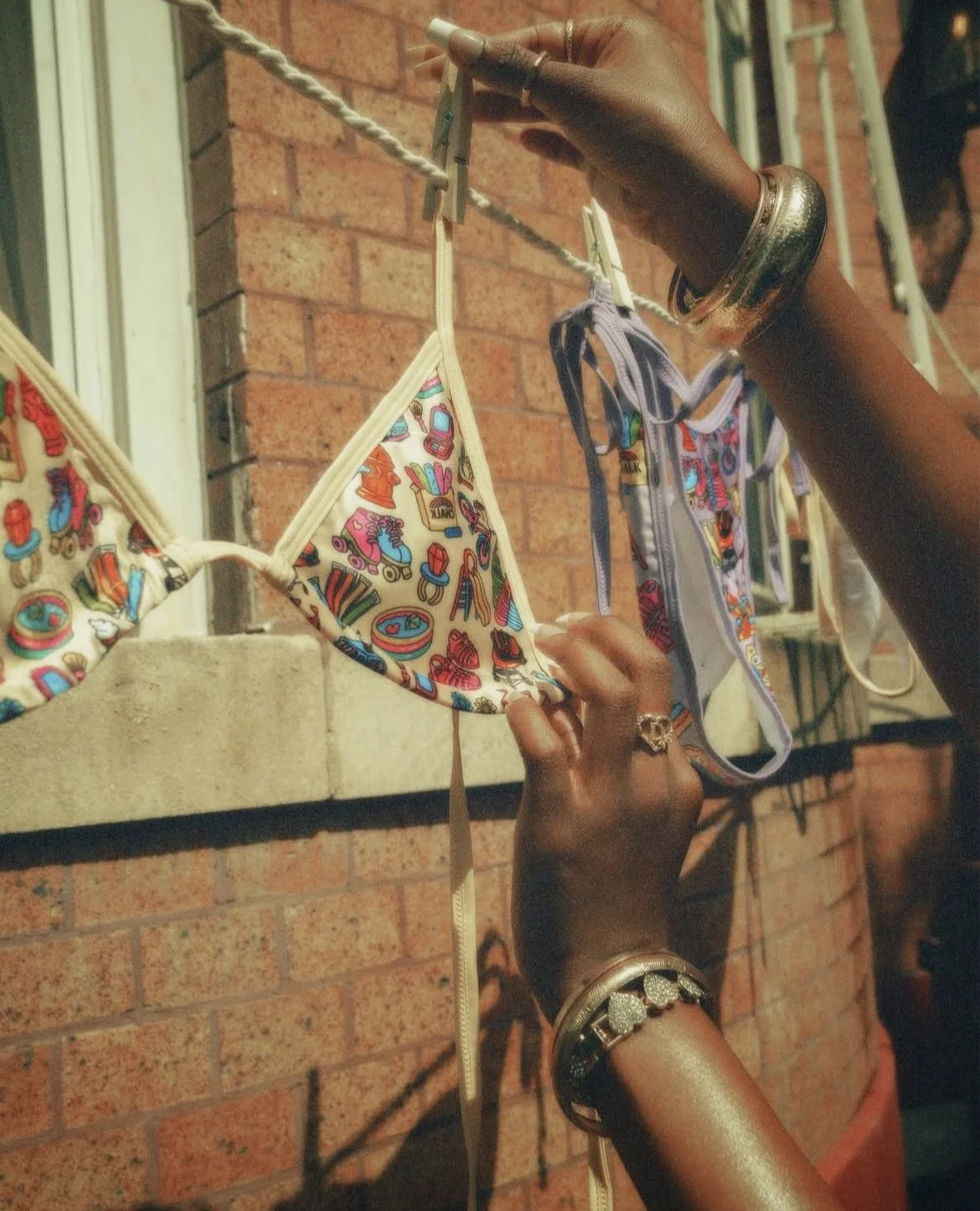 Person hanging colorful bras on a clothesline outside against a brick wall.