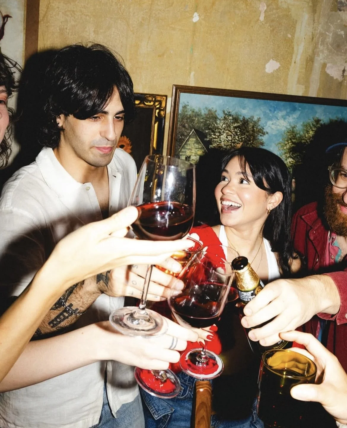 People clinking glasses with red wine, celebrating together indoors.