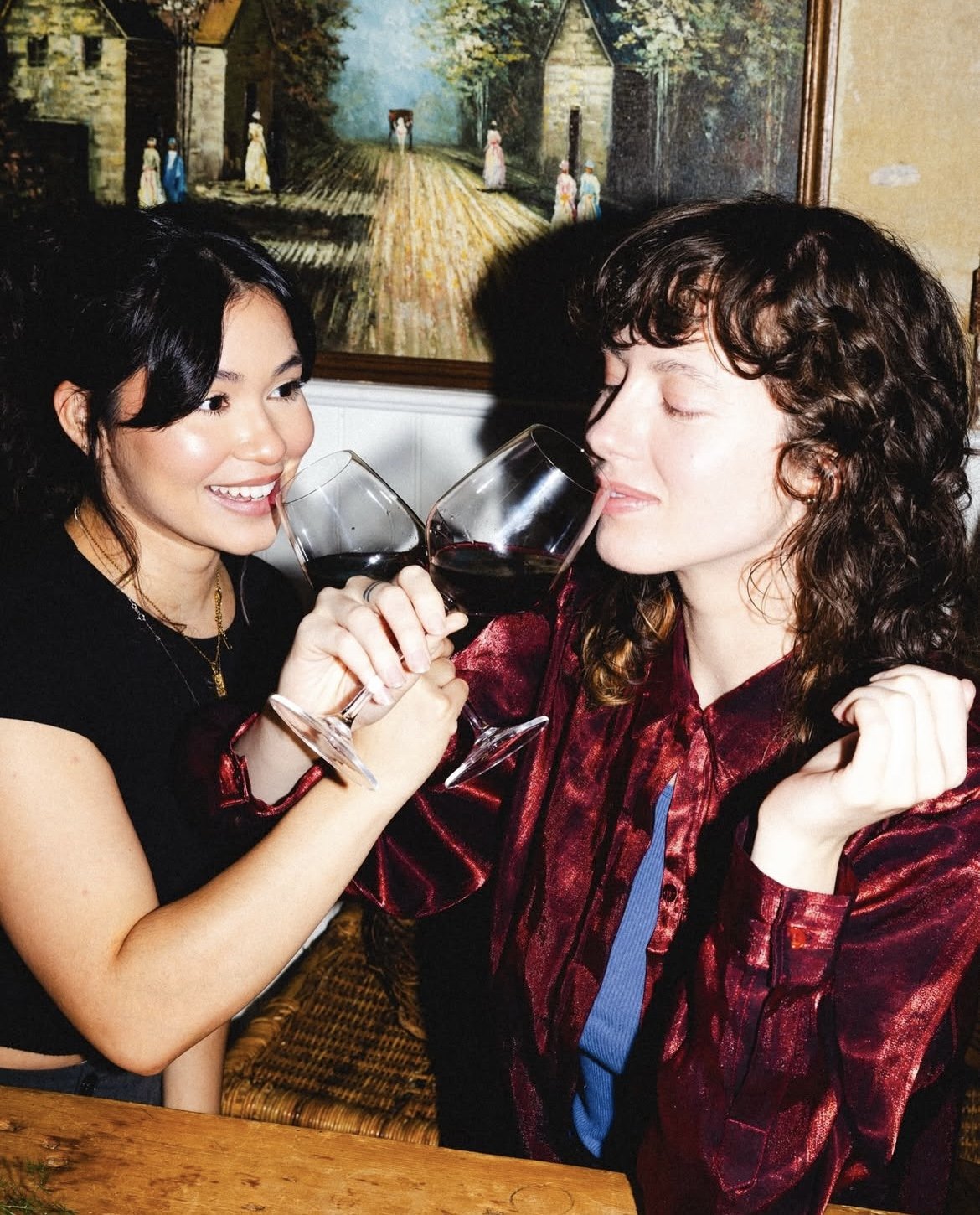 Two women clinking glasses of red wine and smiling at each other.