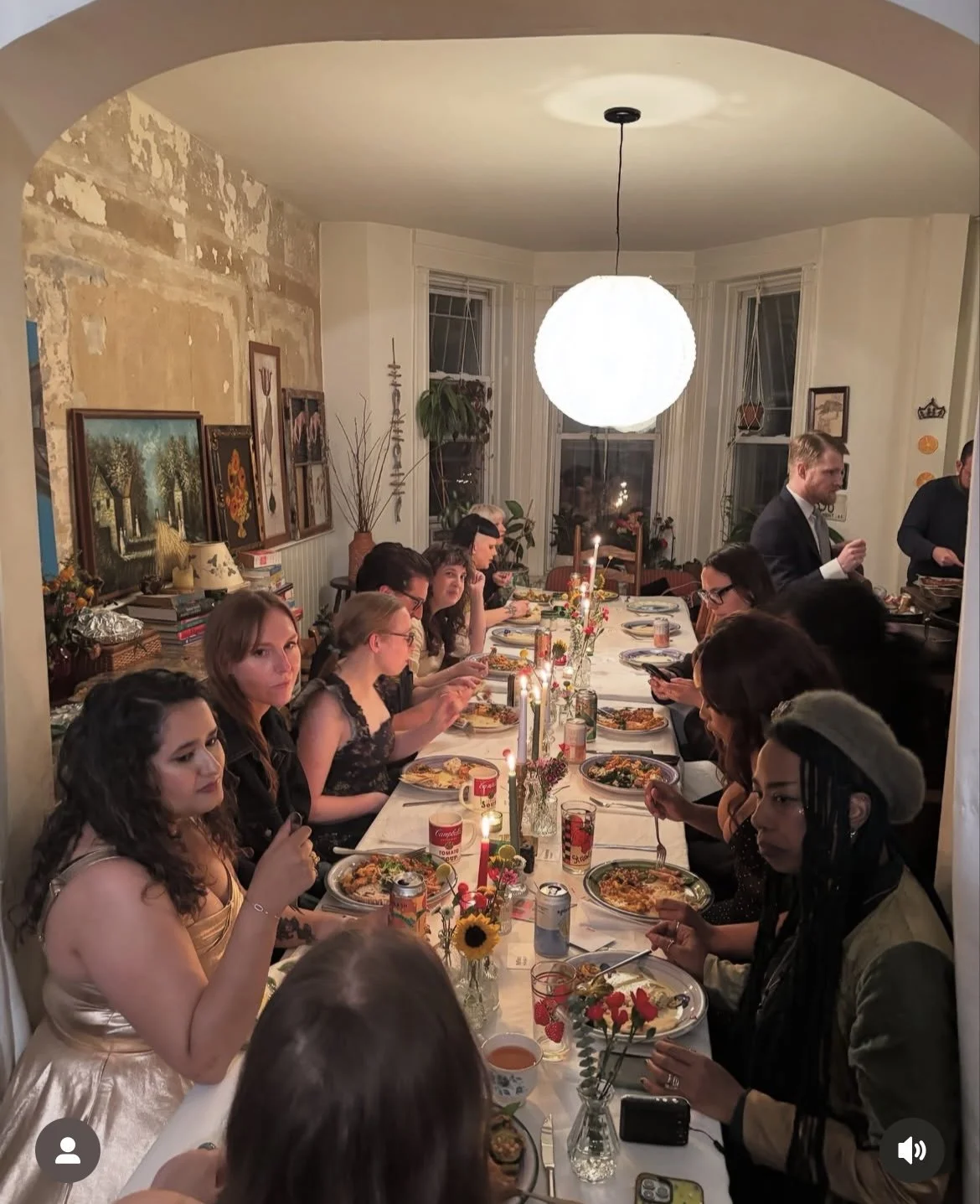 People gathered around a dining table celebrating dinner, with candles and flowers, in a well-decorated living room.