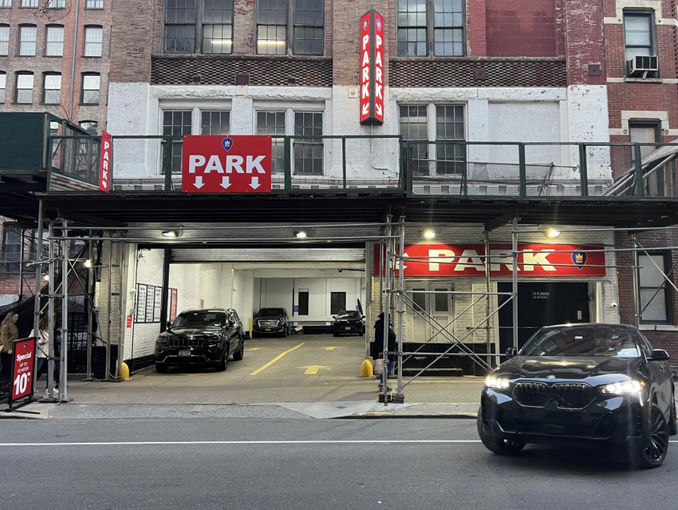 Entrance to an iPark underground parking garage with multiple red and white iPark signs, scaffolding overhead, and cars parked both inside and outside the facility.