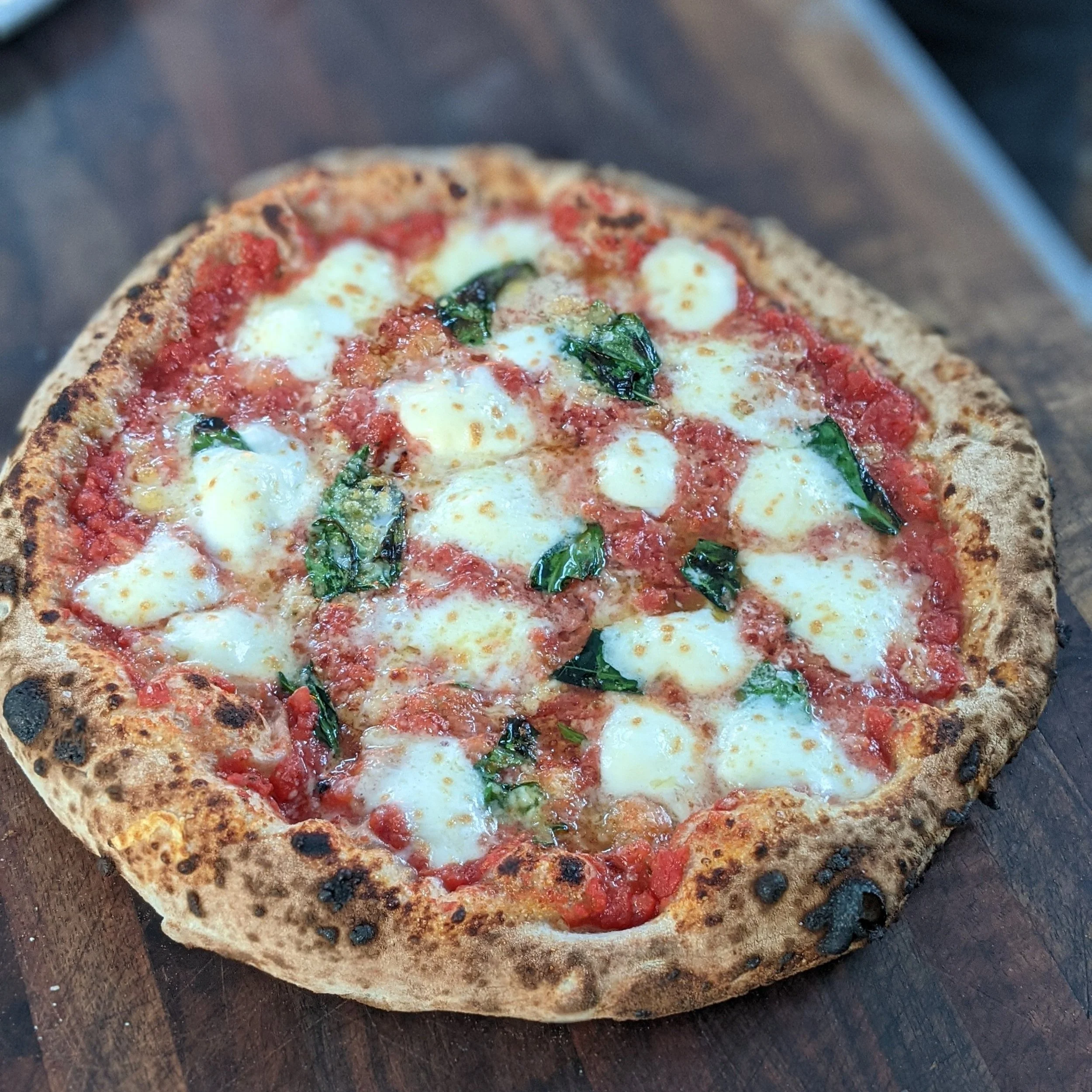 Close-up of a Margherita pizza with tomato sauce, mozzarella cheese, and basil leaves on a wooden surface.