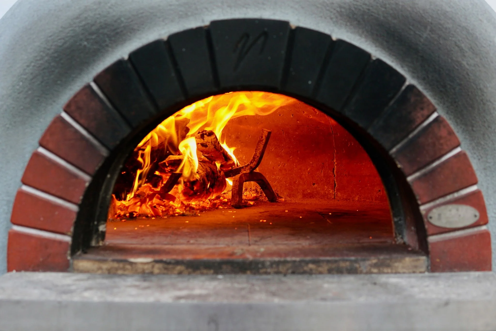 Inside a wood-fired pizza oven with flames and burning logs