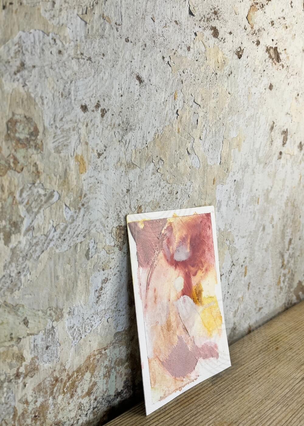 Side view of abstract artwork "Held by Myself No. 10" leaning against a textured wall, showing layered rose and yellow tones with a warm composition.