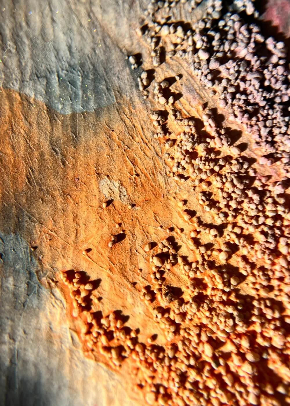Close-up textures reveal burnt orange grains and fluid crimson veins — the earth of emotion transformed by light.