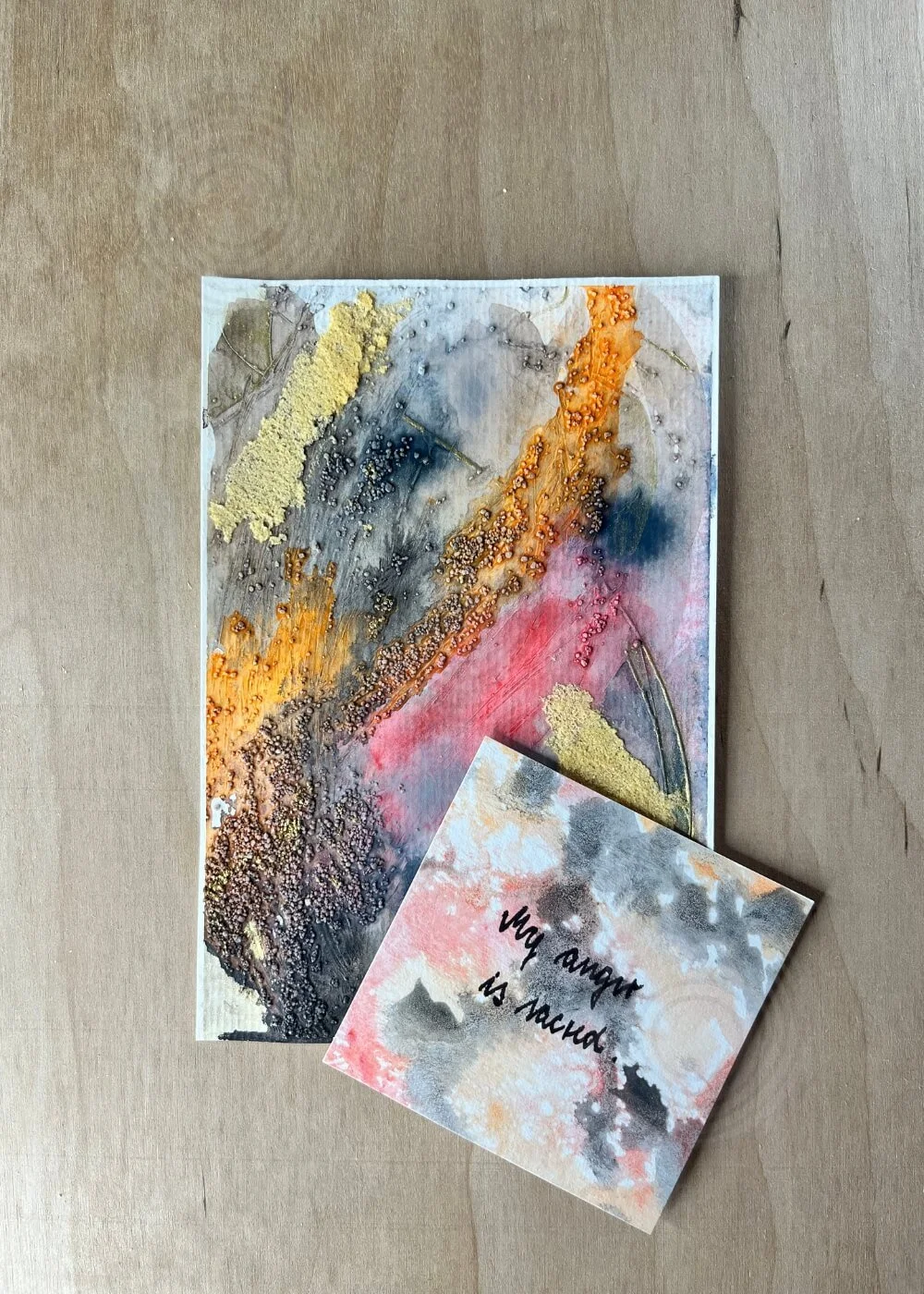 A card beside the piece reads “My anger is sacred.” The phrase breathes through the canvas like forgiveness found in flame.