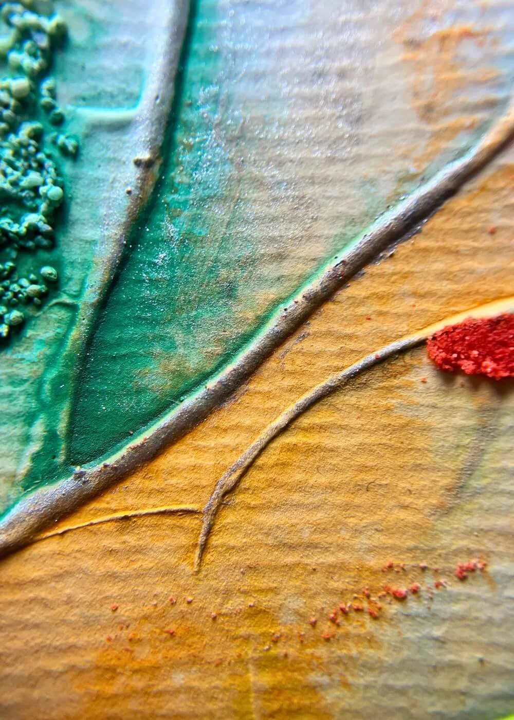 Close-up of green and orange textured layers from Risen through fire, showing fine line engravings and tactile depth.