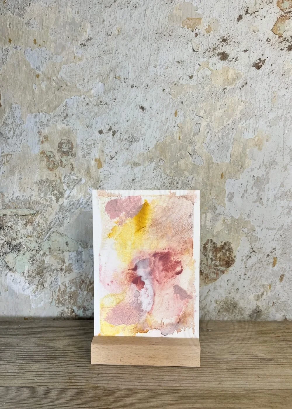 Abstract artwork “Held by Myself No. 8” displayed on a wooden stand, featuring warm tones of golden yellow, soft rose, and deep burgundy against a textured background.