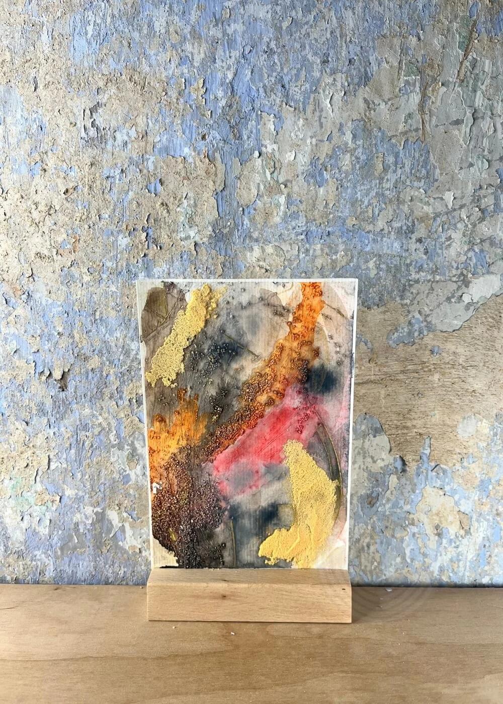 A textured painting stands in quiet strength — golden dust, ash-grey, and ember-red forming a map of healing across the surface.