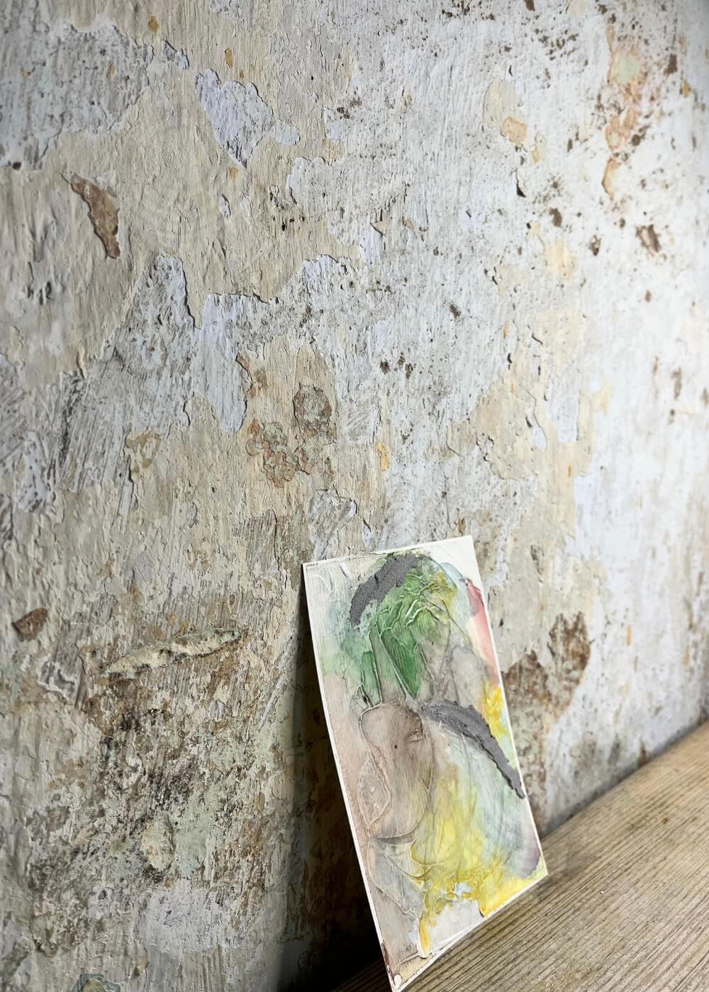 Close view of the same abstract painting "Between the Seconds No. 10"  leaning against a rustic, weathered wall, showing layered textures and muted colors.