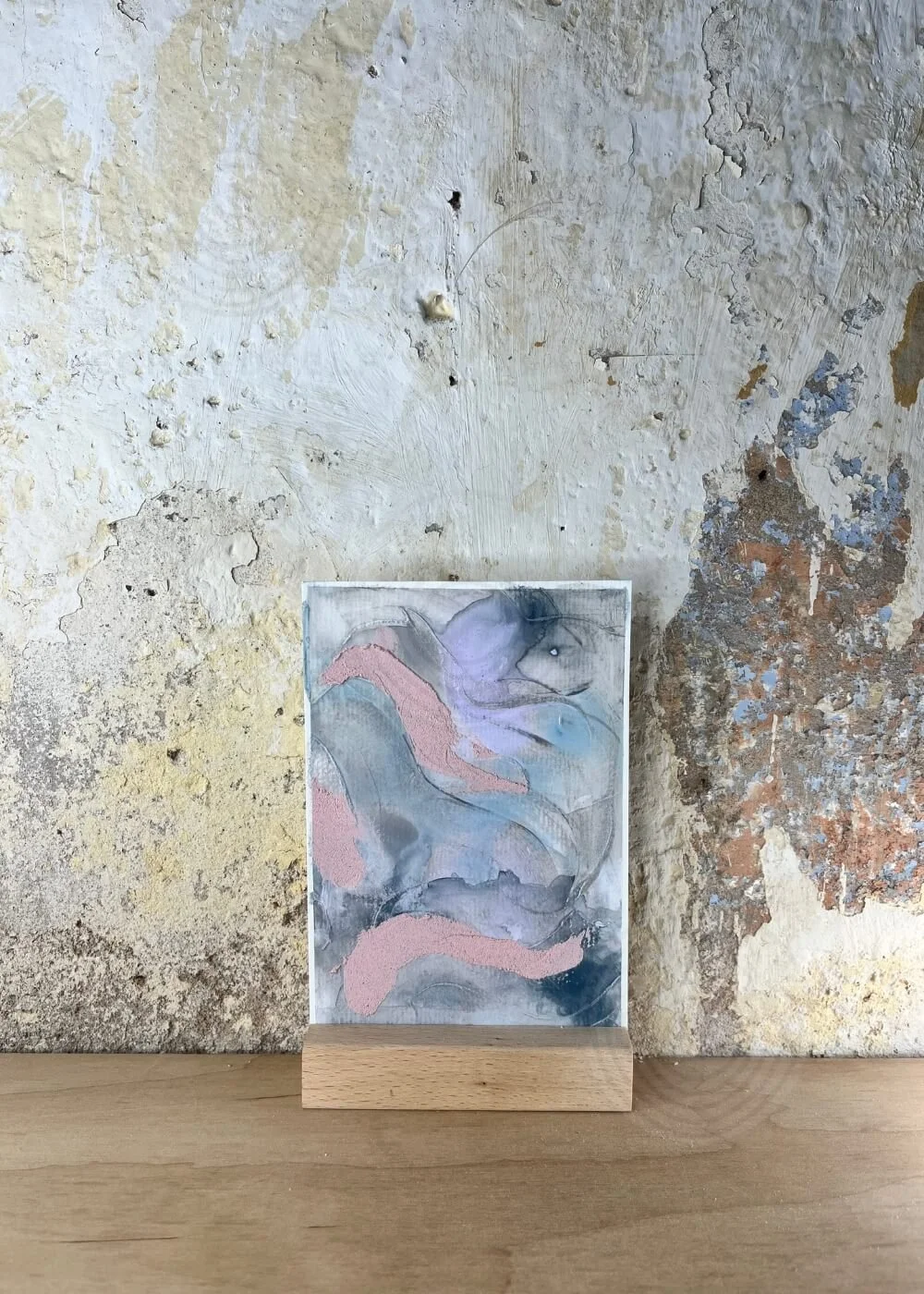 Textured abstract artwork in blush, blue, and lavender tones from the Between Breaths series — Beneath the Surface, It Keeps Flowing, symbolizing calm motion and emotional depth.