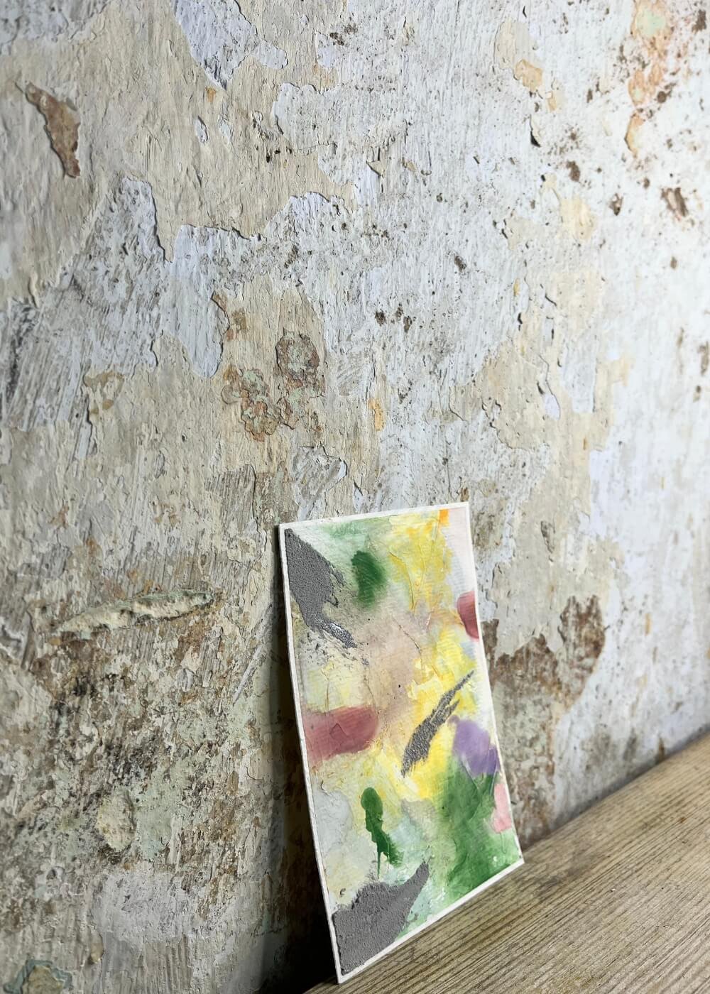 Side view of the abstract artwork Between the Seconds – No. 3 leaning against a textured wall, showing layered tones of yellow, green, violet, and grey.