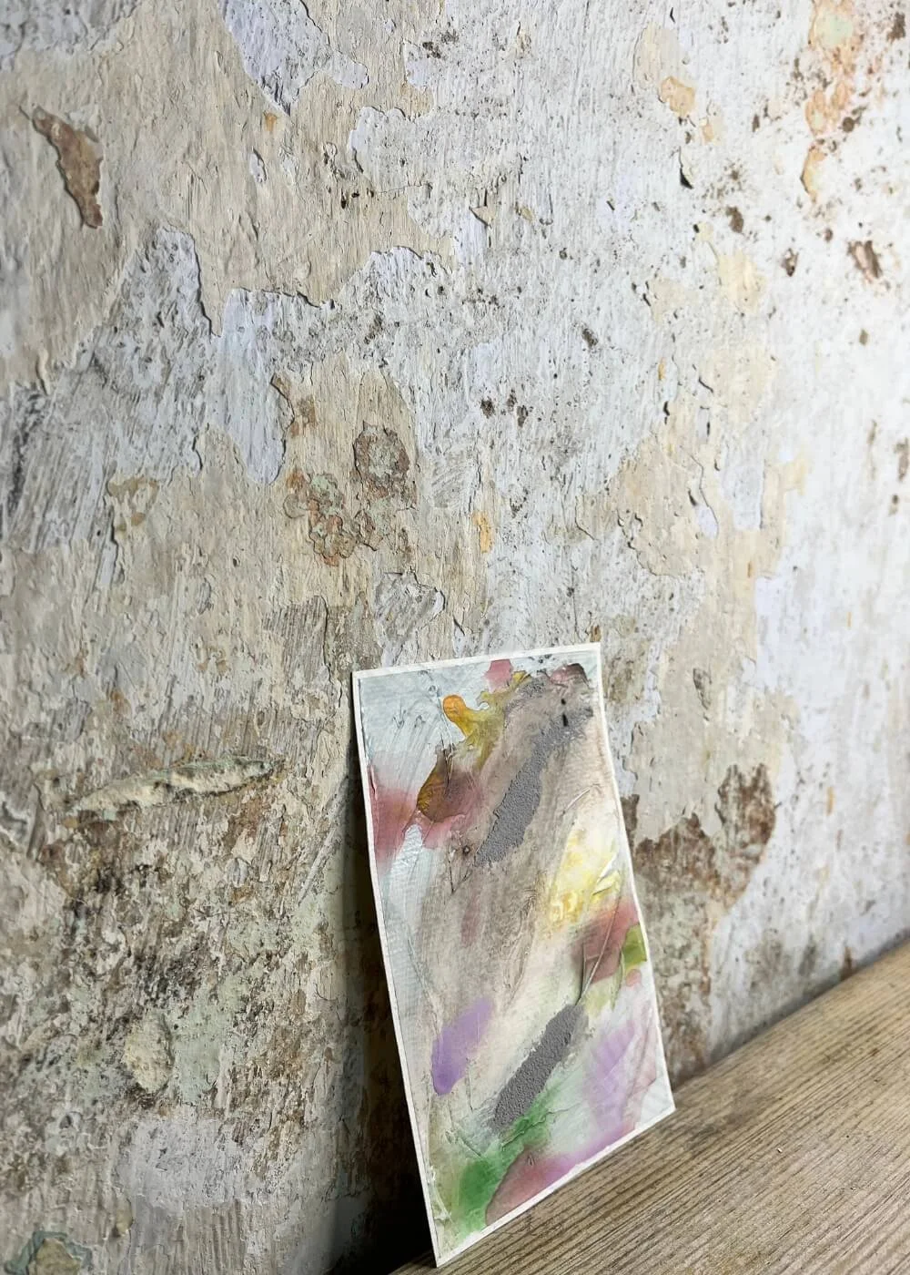 Side view of the abstract artwork Between the Seconds No. 5 showing layered textures in pastel green, lavender, and yellow against a rustic wall.