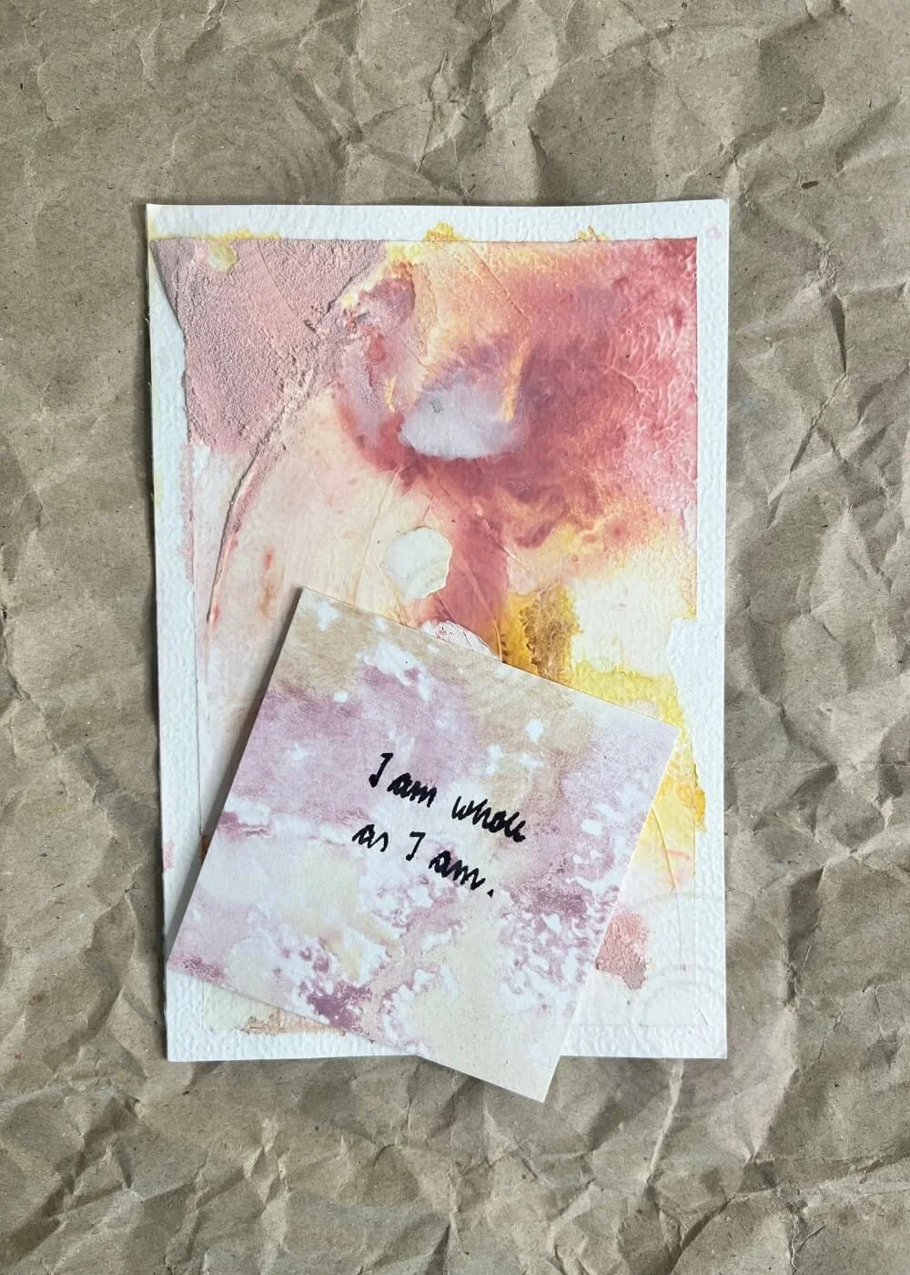Abstract artwork "Held by Myself No. 10" on kraft paper background with a handwritten affirmation card reading 'I am whole as I am.' placed on top.