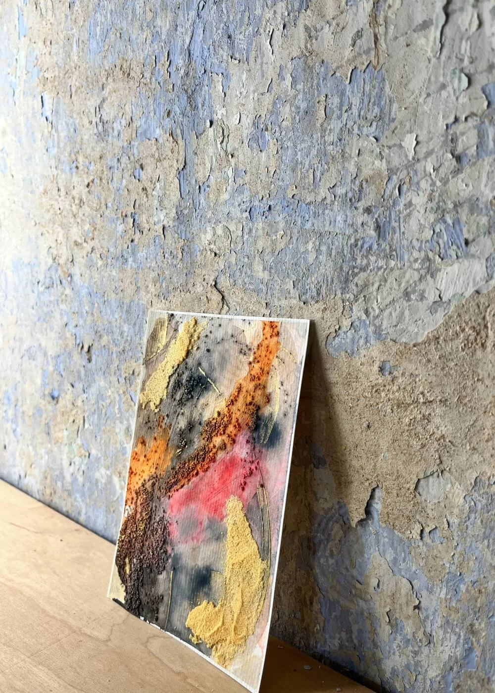 The artwork leans softly against a worn wall — its scarred hues telling stories of endings that became new beginnings.