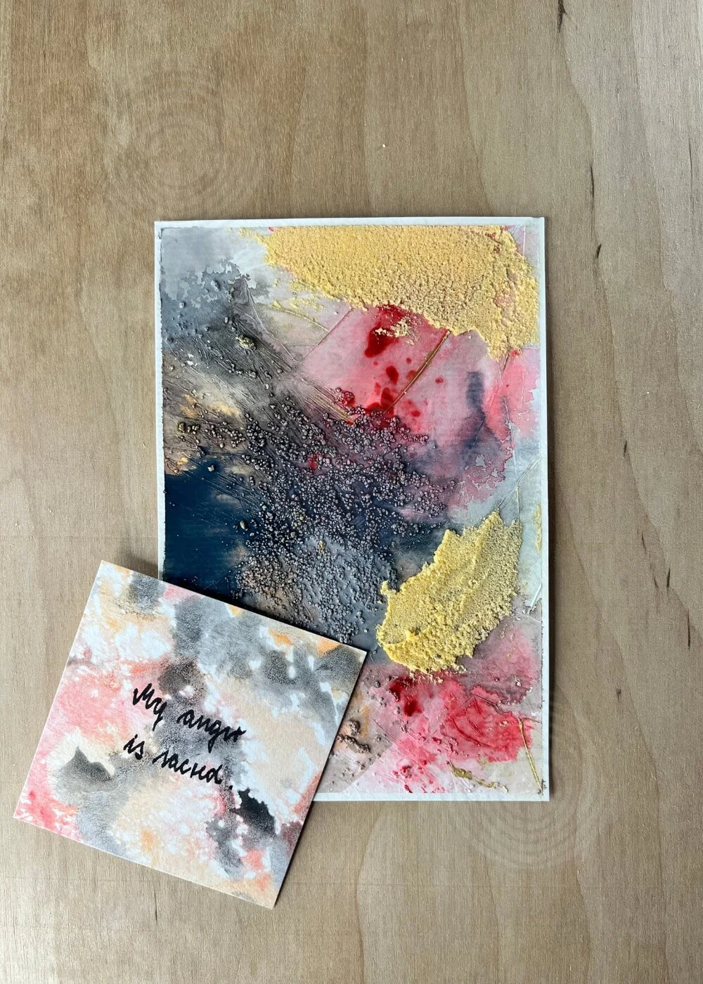 A card beside the artwork reads “My anger is sacred.” The message hums through red textures and golden dust, like truth reborn in silence.