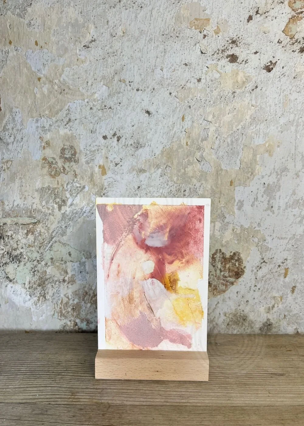 Abstract artwork "Held by Myself No. 10" displayed in a wooden stand, featuring soft rose and golden yellow textures with organic flowing forms.