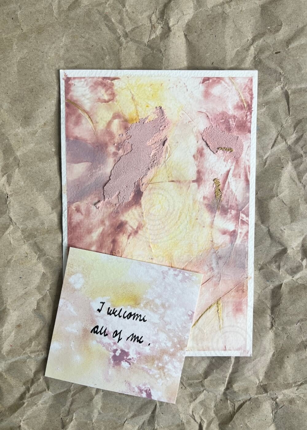Abstract postcard-sized artwork in soft rose and gold, shown alongside an affirmation card that gently states “I welcome all of me.”