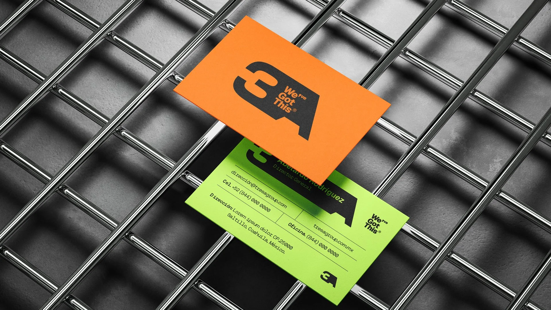 Tarjetas de presentación sobre una rejilla metálica, una de color naranja con el logotipo 'We've Got This' y otra verde con información de contacto.